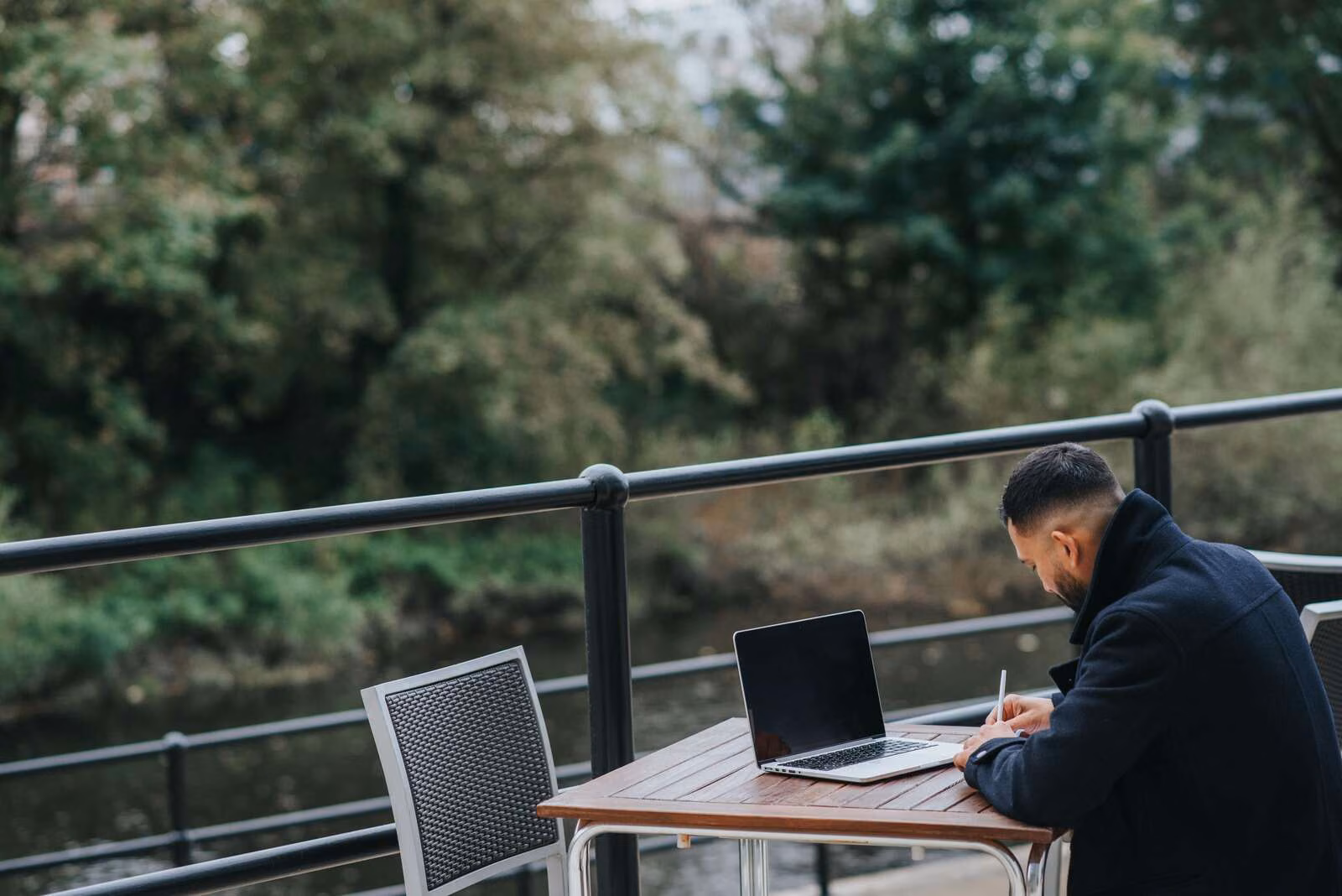 Iemand die op afstand werkt maakt aantekeningen naast een geopende laptop aan een tafel buiten